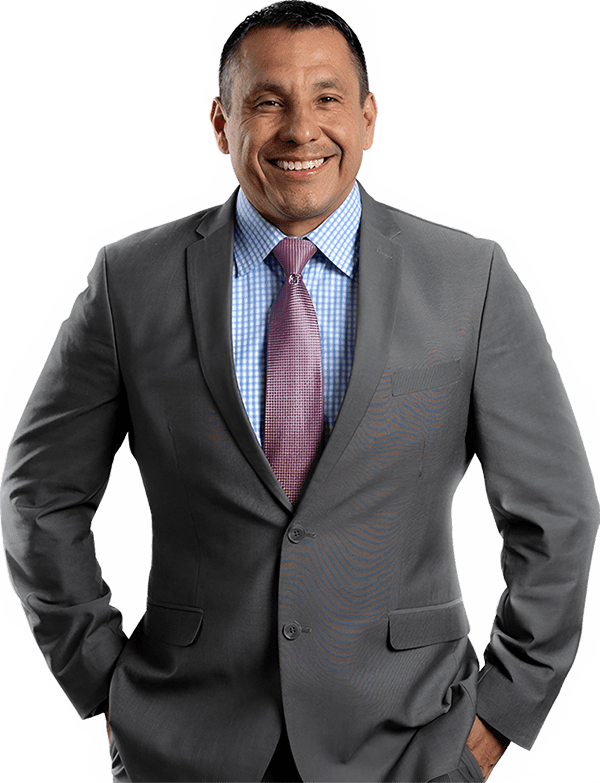 Daniel Gomez in a gray suit Daniel Gomez wearing a gray suit over a blue checkered shirt with a pink tie stands with their hands in their pockets and smiles at the camera, giving us a glimpse of their confident style.