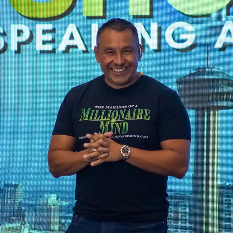 Daniel Gomez is smiling and clasping his hands in front of him while wearing a black T-shirt that reads "The Makings of a Millionaire Mind". He stands against a backdrop of a city skyline featuring the Space Needle, embodying the confidence that stems from effective coaching. Daniel Gomez is smiling and clasping his hands in front of him while wearing a black T-shirt that reads "The Makings of a Millionaire Mind". He stands against a backdrop of a city skyline featuring the Space Needle, embodying the confidence that stems from effective coaching.